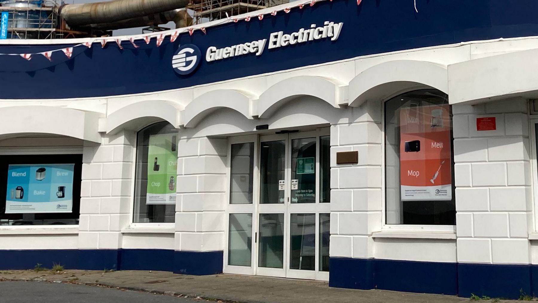The front building of Guernsey Electricity - the sign above the glass double door, with three windows in vision. The building is painted striped blue and white.