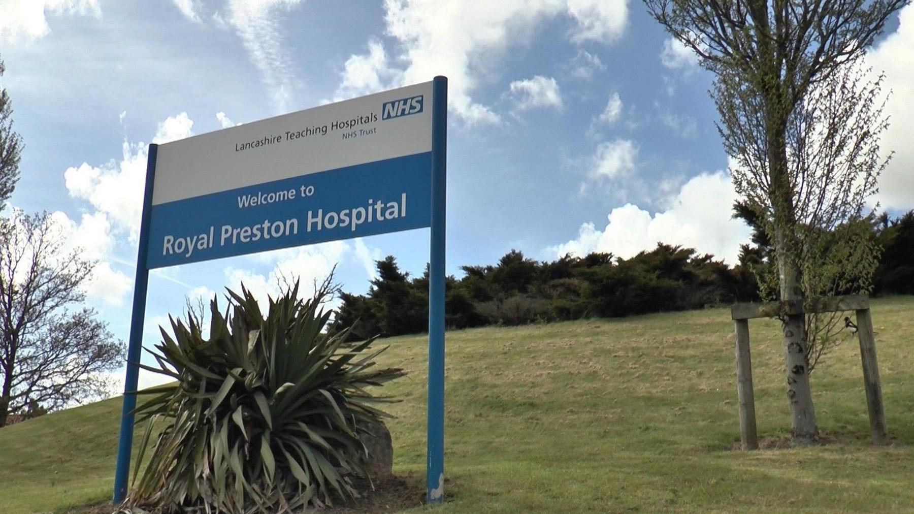 A sign on a grass verge says 'Welcome to Royal Preston Hospital'.