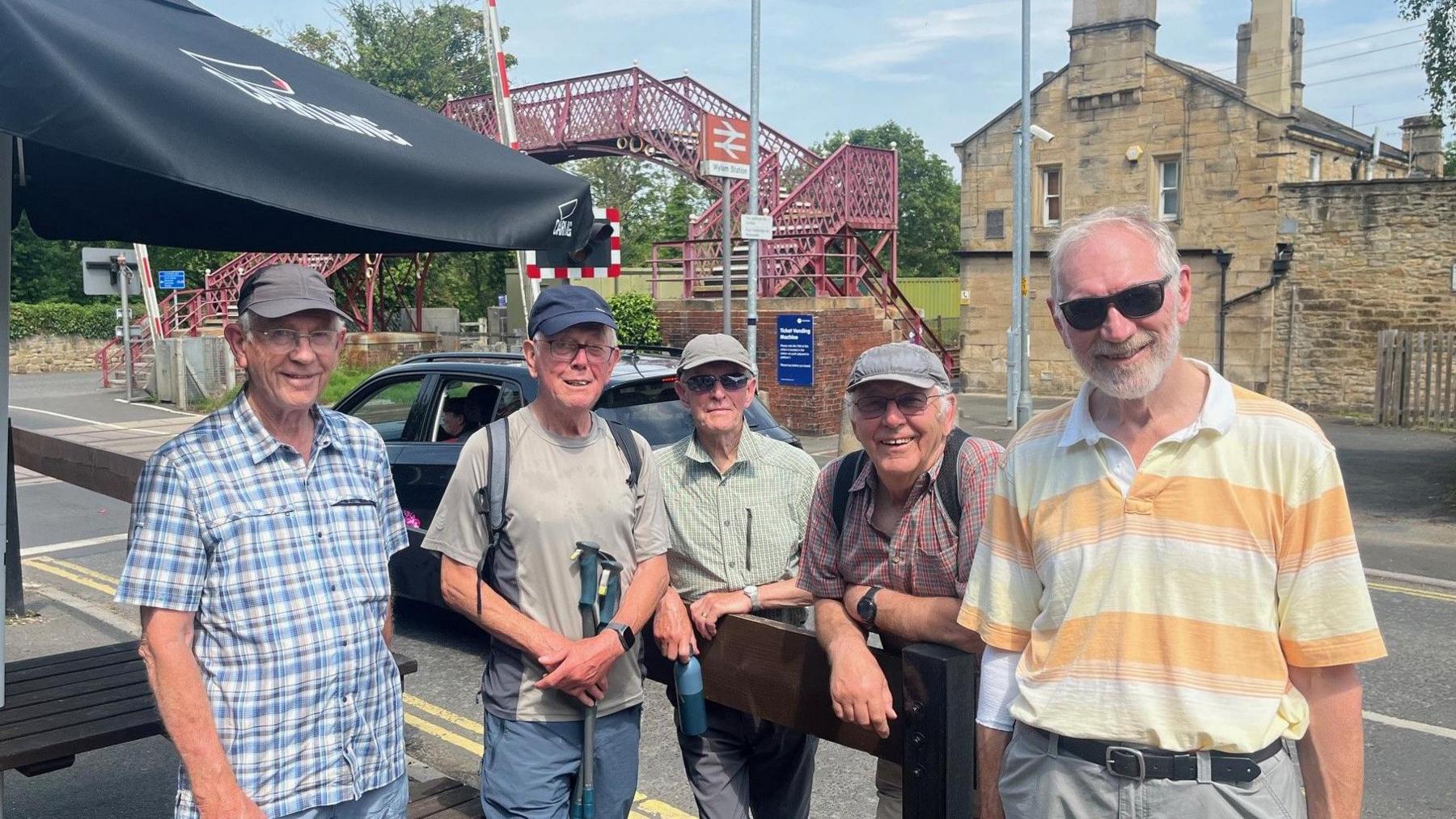 Frank Phillips, Peter Etherington, Rob Doughty, Tony Evans and Gerry Slater standing it front of a railway bridge in the sun. They are all smiling in a beer garden wearing short-sleeve tops.