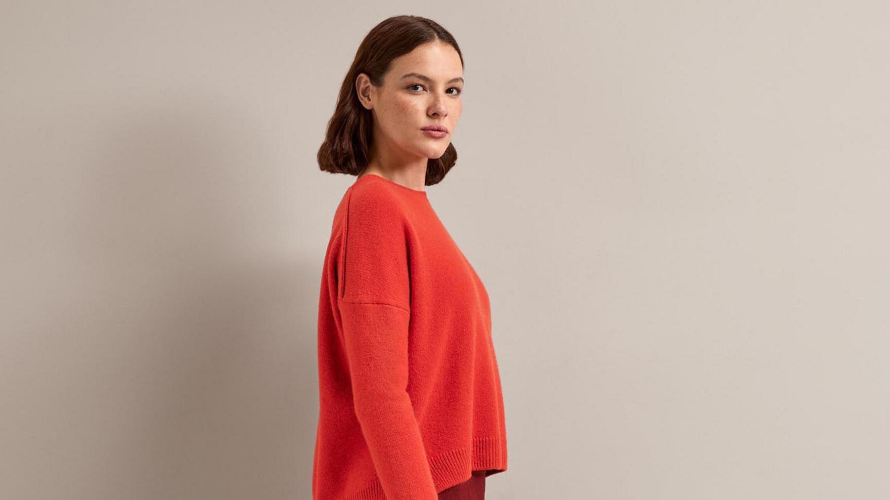 A Cefinn model looks at the camera. She has shoulder-length brown hair and wears an orange jumper with natural-looking make-up.