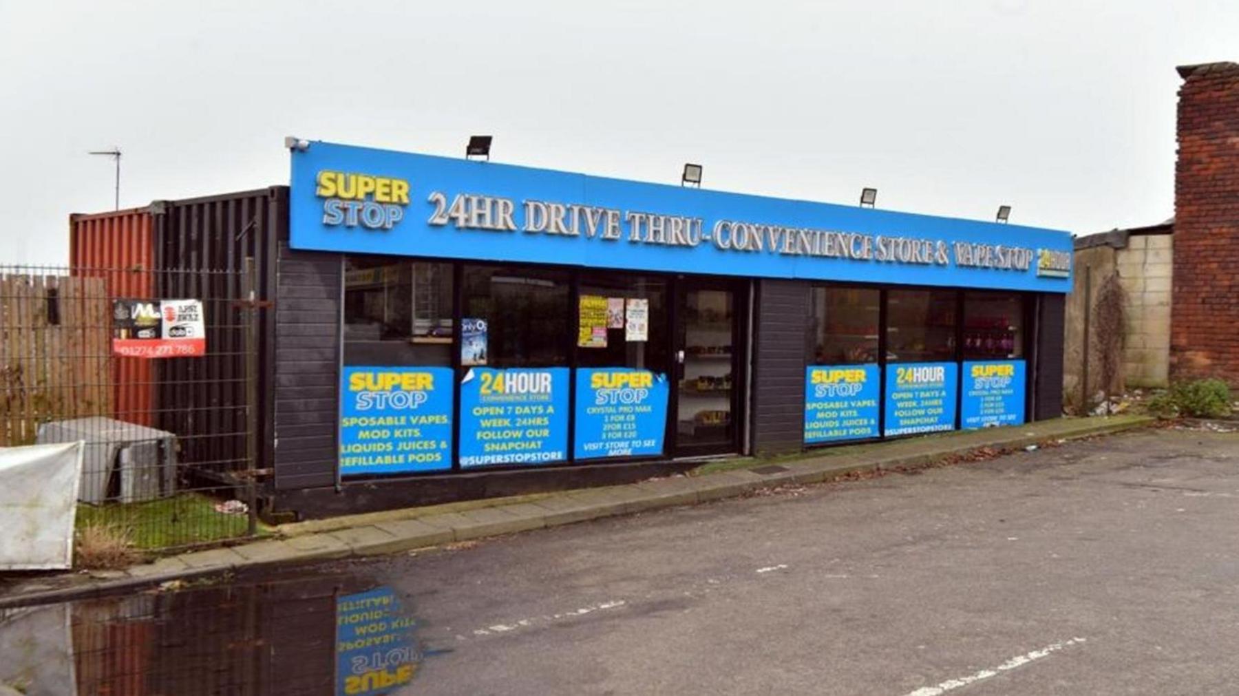 The front of the drive thru store, which is located inside two shipping containers which have been joined together. The shops sign reads 'Super Stop 24HR drive thru convenience store and vape shop'.