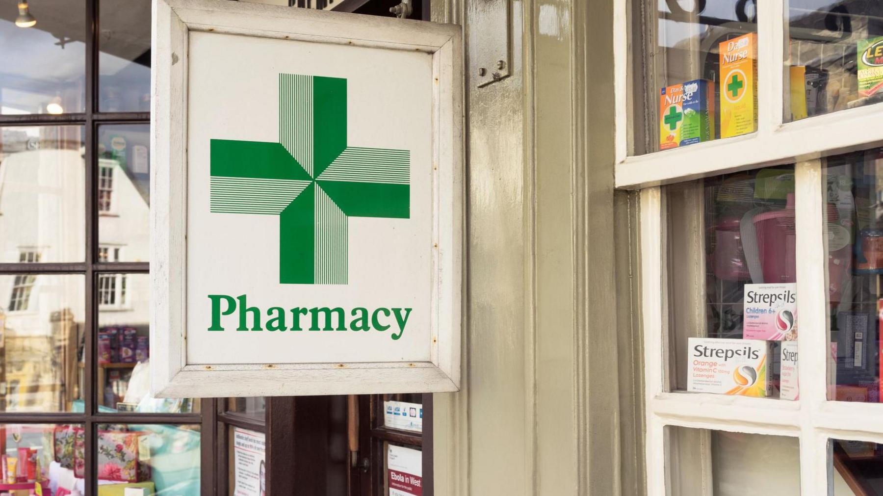 A wooden sign, depicting the traditional green pharmacy cross, on a small, community pharmacy in England 