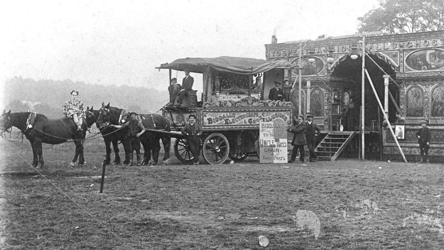 An old image of a fairground ride with horses and show people