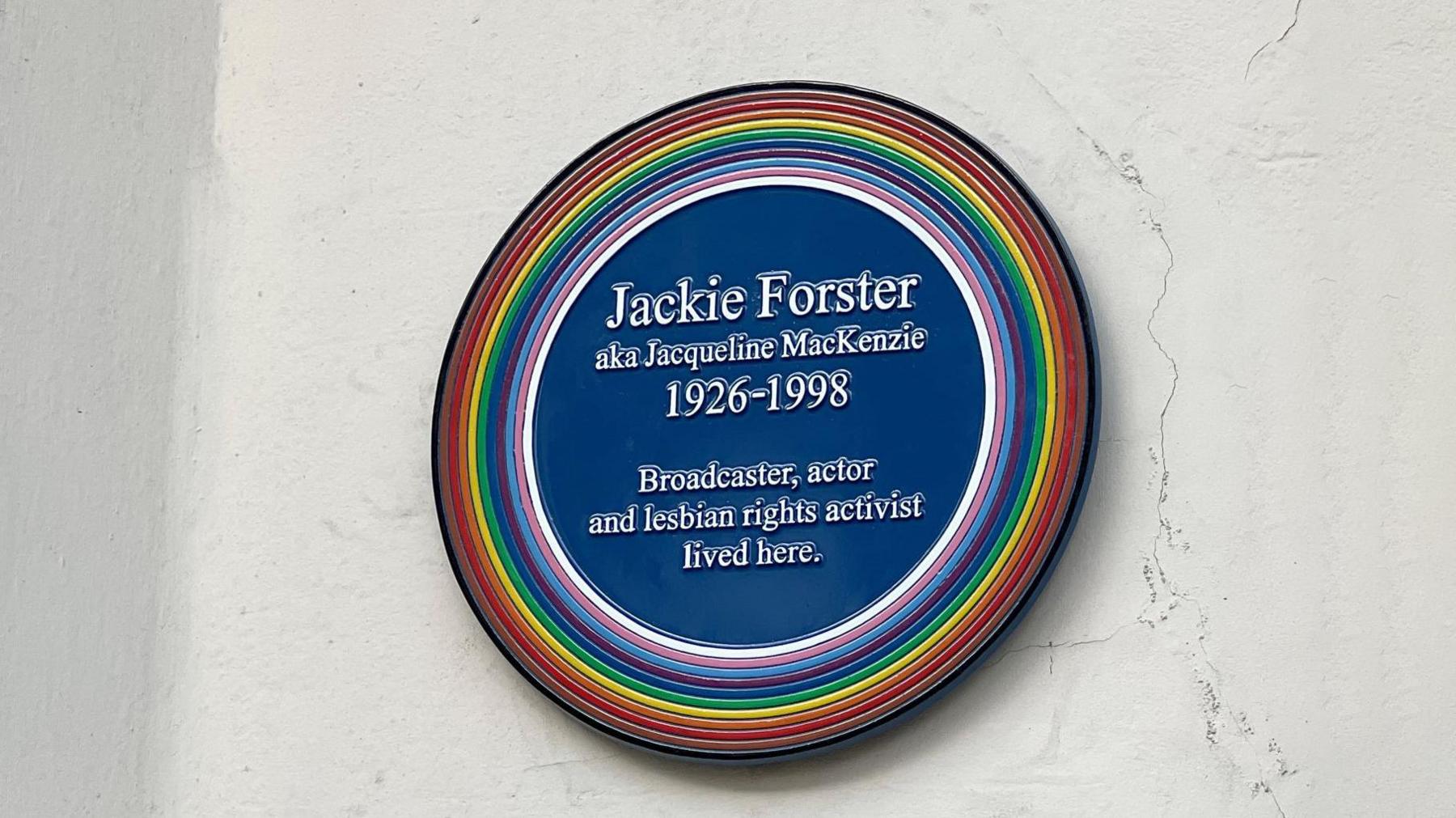 A blue commemorative plaque with rainbow colours round it