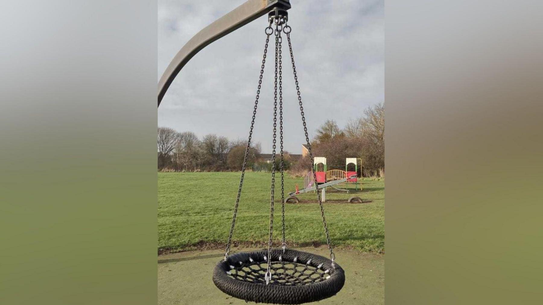 The swing at The Willows. It is a basket-type swing. The basket is black. It is fixed to the hoist by four chains. 