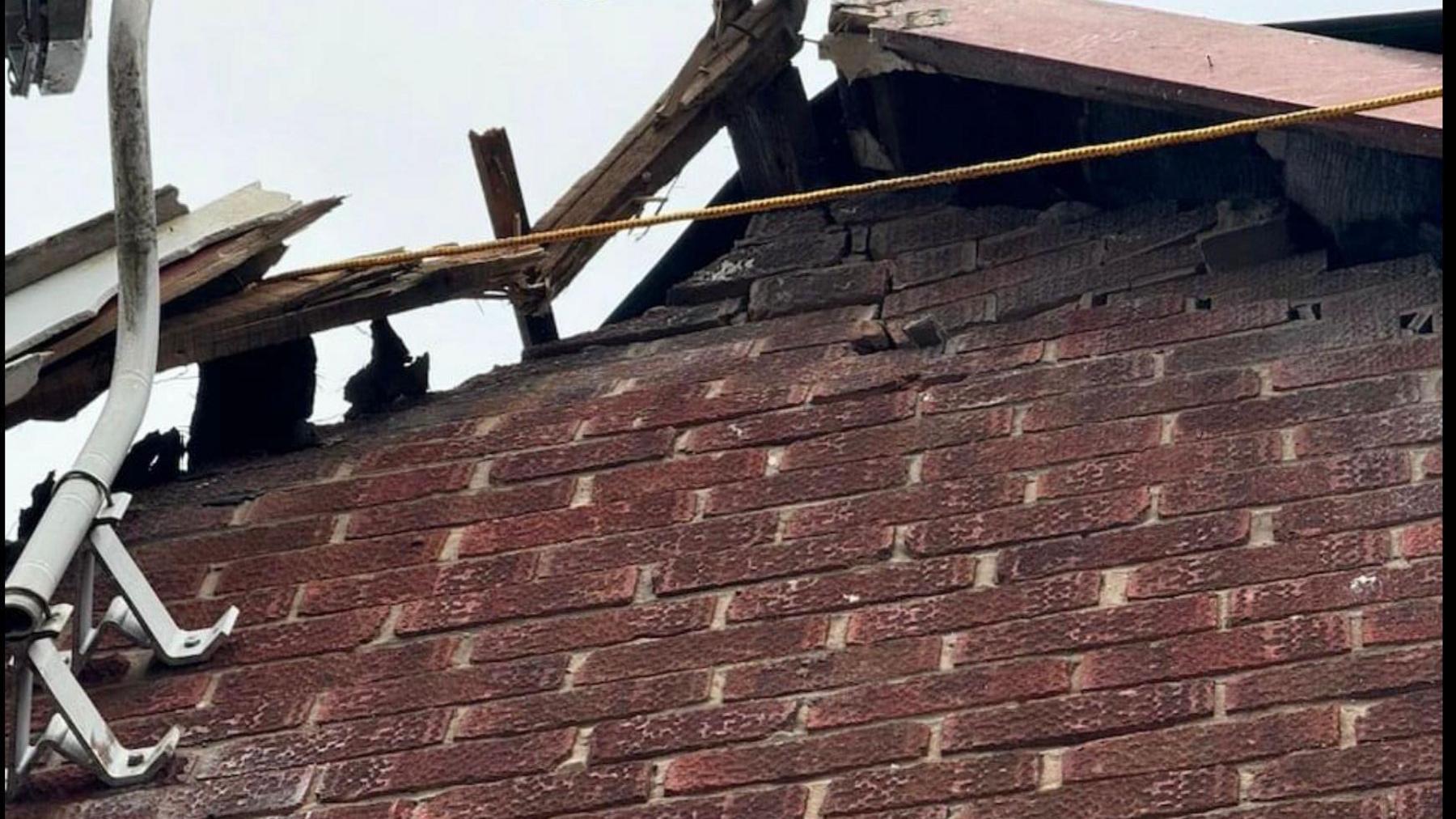 The side of a house with damaged brickwork and a broken roof section.