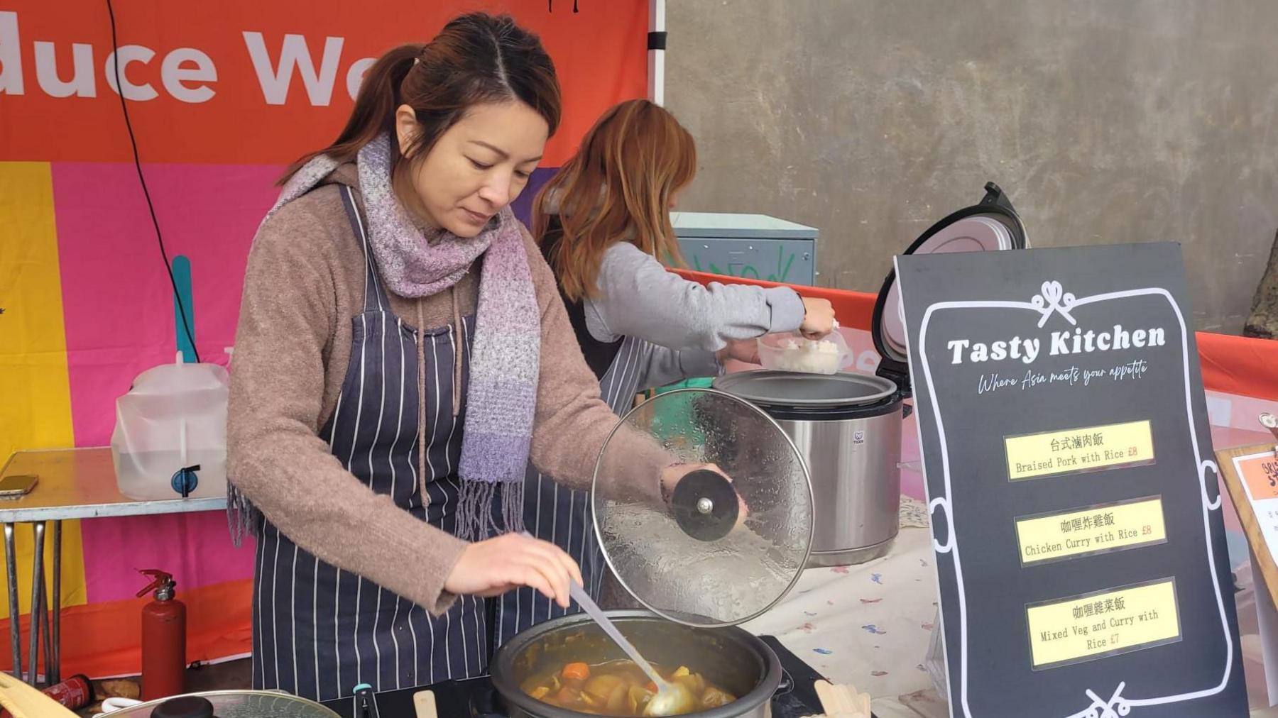 Jenny Luk stirring a pot with curry in it, behind a food stall outside.