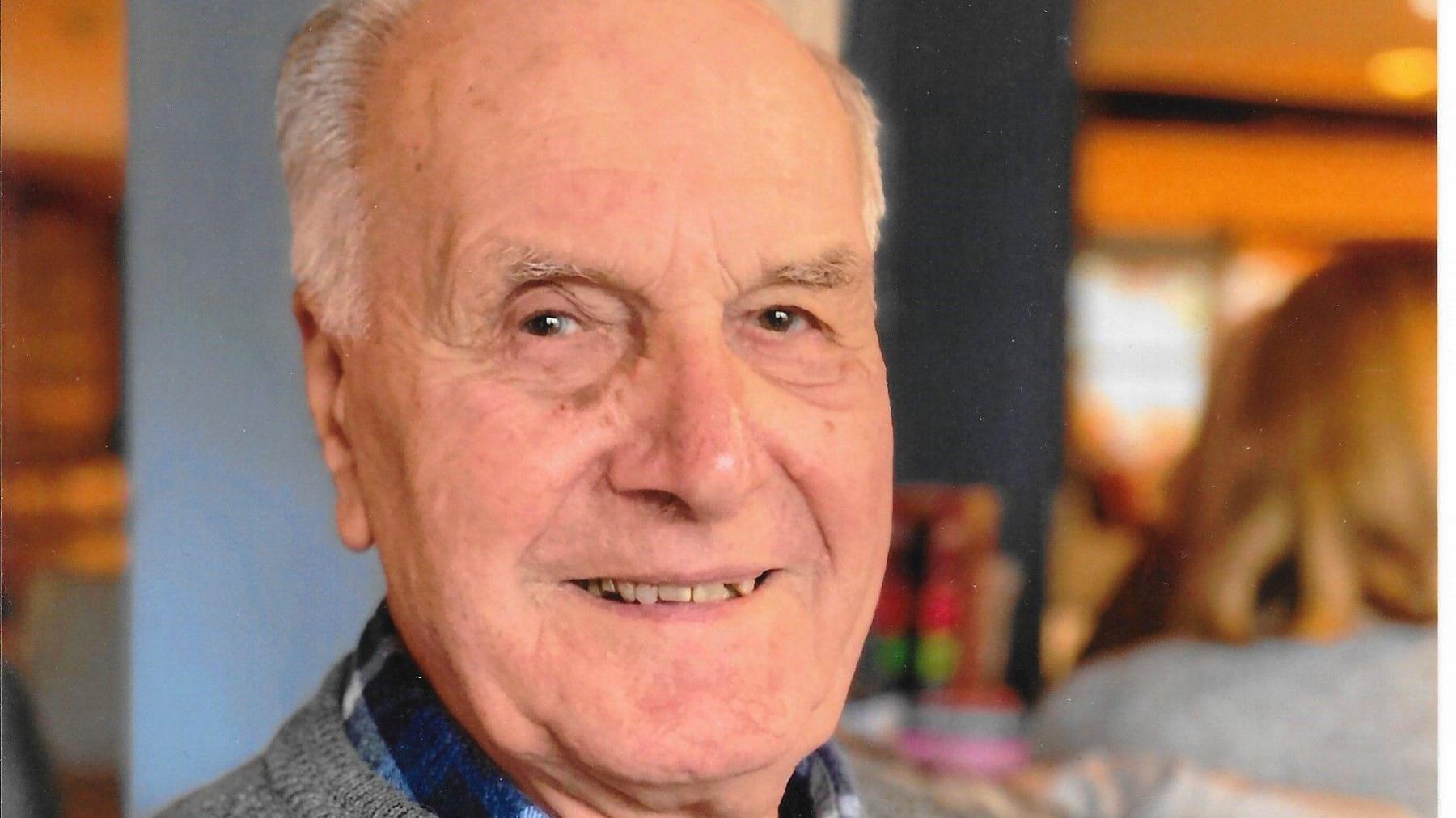 Donald Butt is seen from his shoulders up. He is smiling and wearing a grey jumper over a blue shirt.