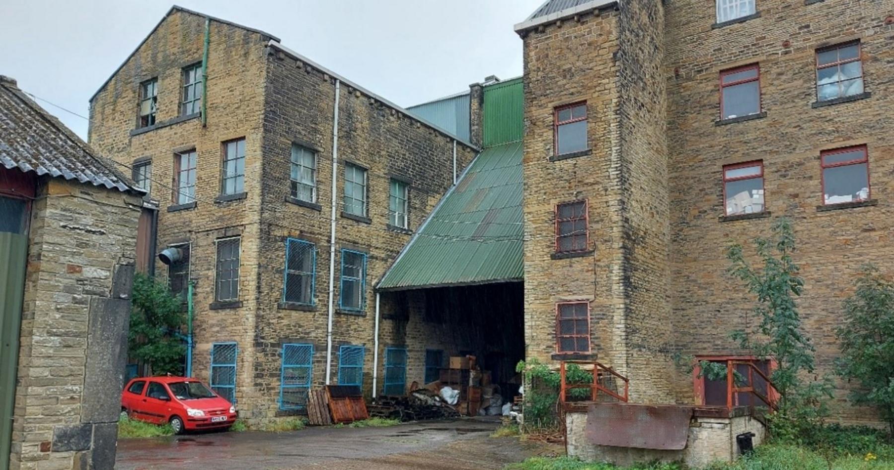 The back of the former Victor Works woollen mills on Bolton Hall Road in Bradford which could be turned into flats. A red car is parked close to part of the building which has a green sloping iron roof.