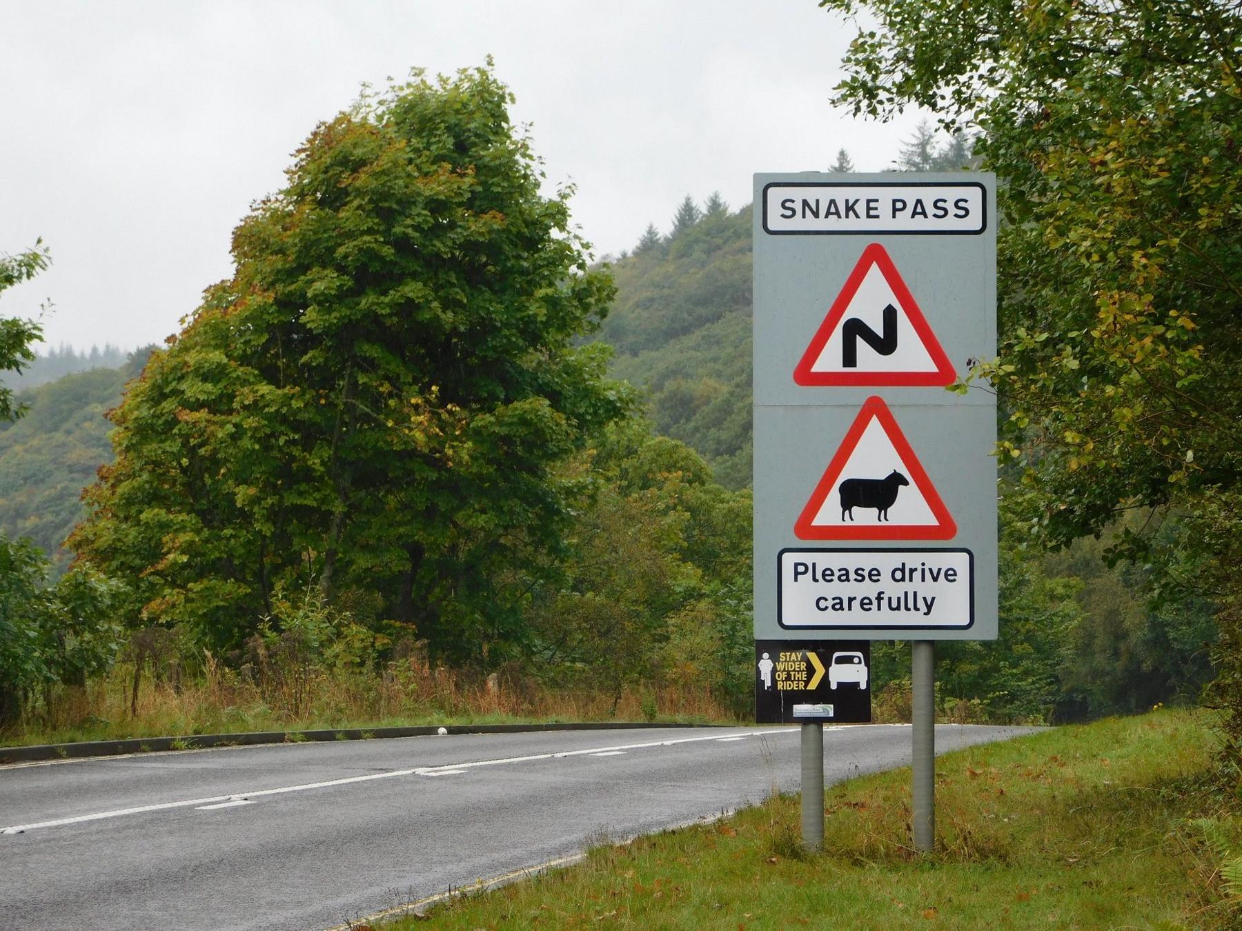 A sign for Snake Pass warning of winding roads and livestock