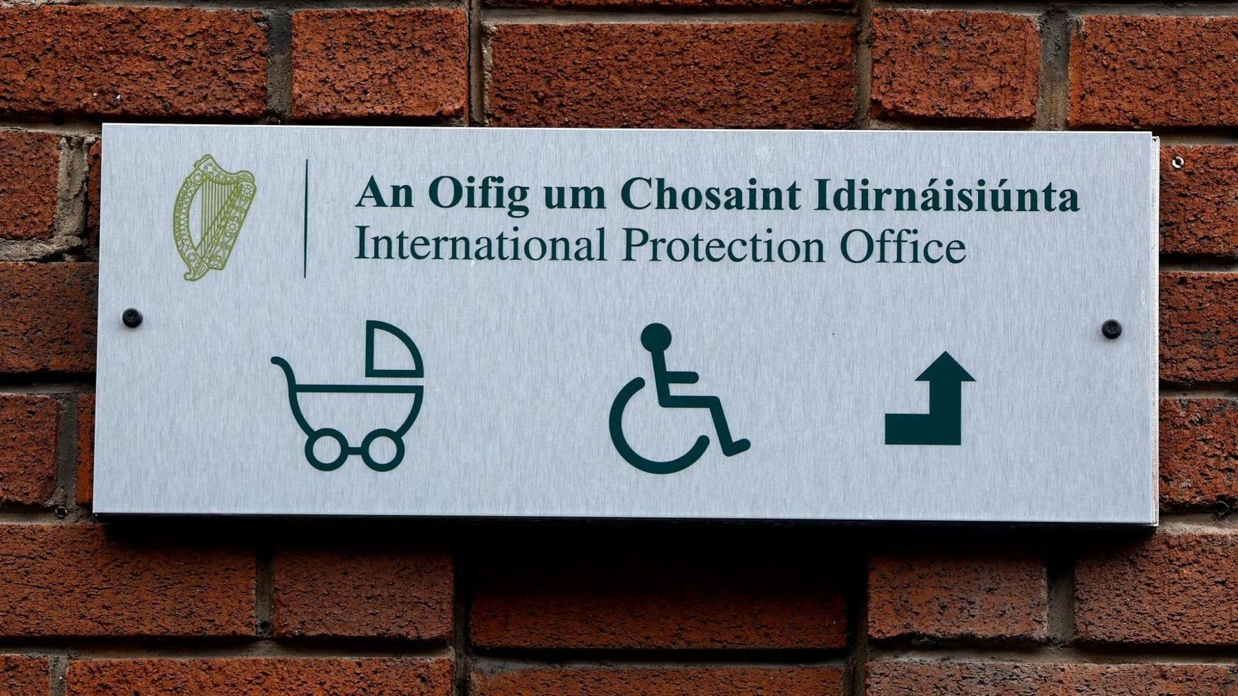 The exterior sign of the International Protection Office in Dublin. The sign shows a icon of a pram, a wheelchair user and an arrow pointed up.