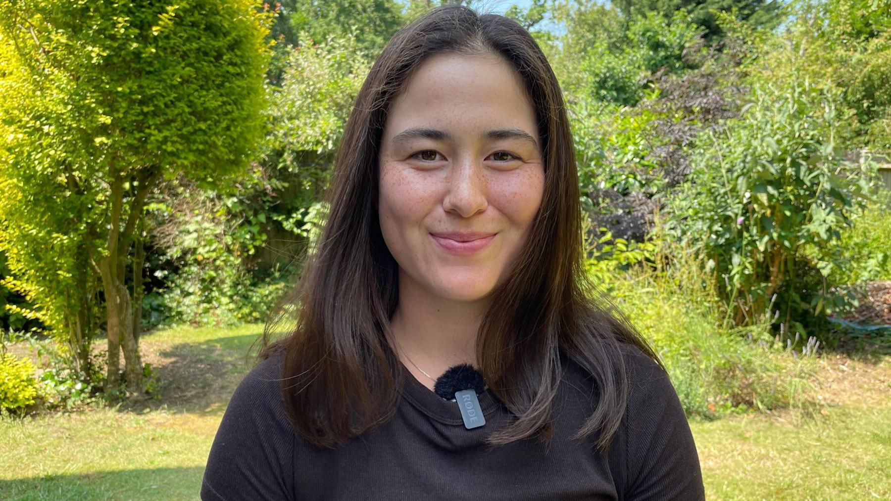 Joanna Garland sits down in a black shirt in a garden setting