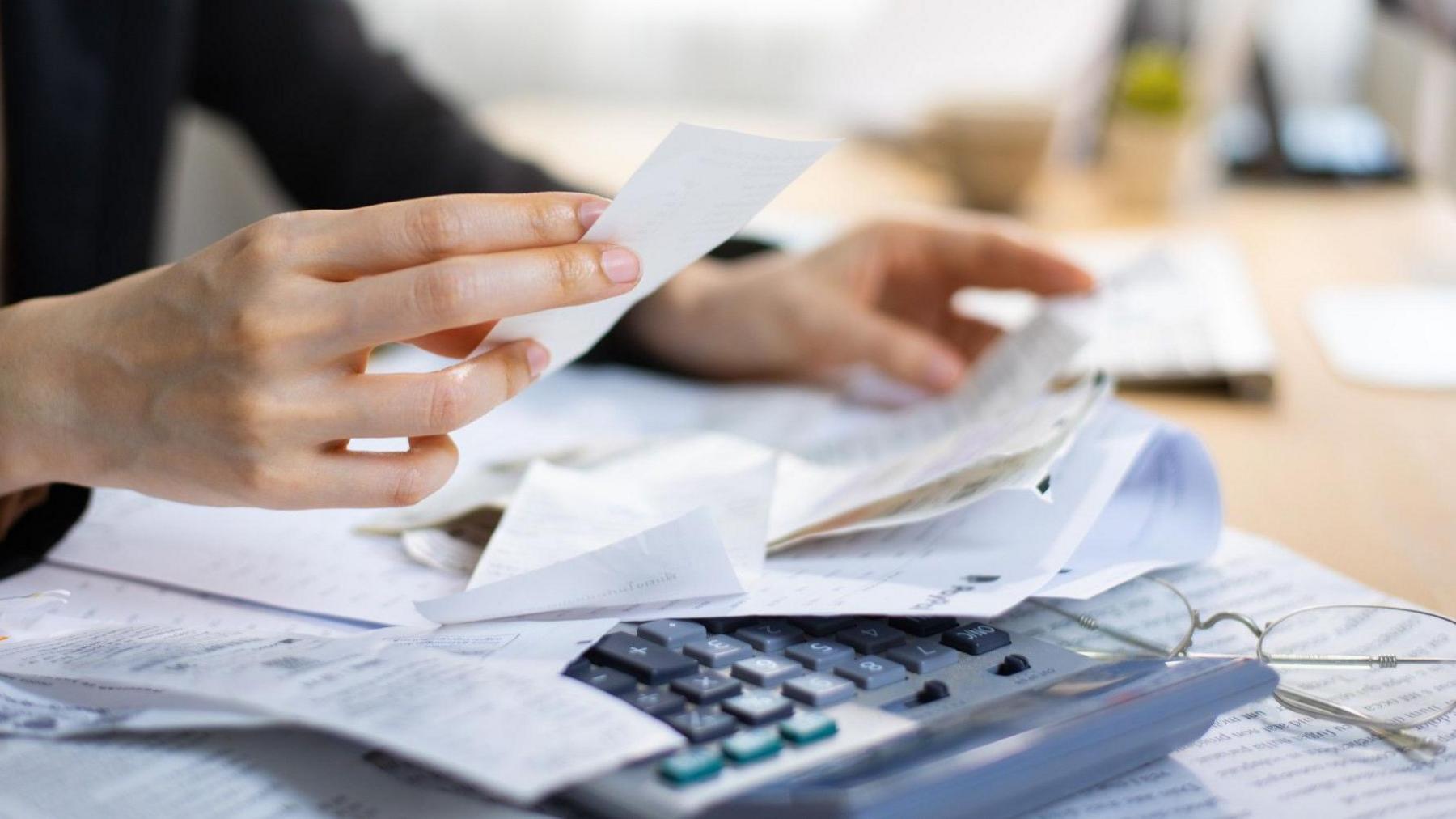 Person holding a receipt alongside a pile of bills and a calculator  