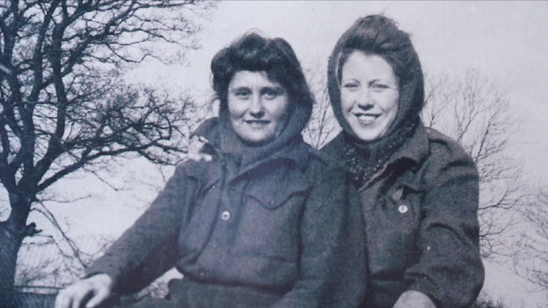 Black and white photo of two Land Army girls in scarves and warm winter clothes.