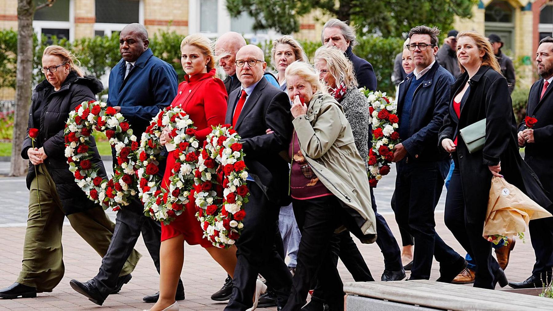 Deputy Prime Minister David Lammy, Justice Minister Alex Davies-Jones and Attorney General Lord Richard Hermer walk down a street alongside Hillsborough campaigners and families with colourful wreaths in their hands as they approach the Hillsborough memorial at Anfield on Monday.