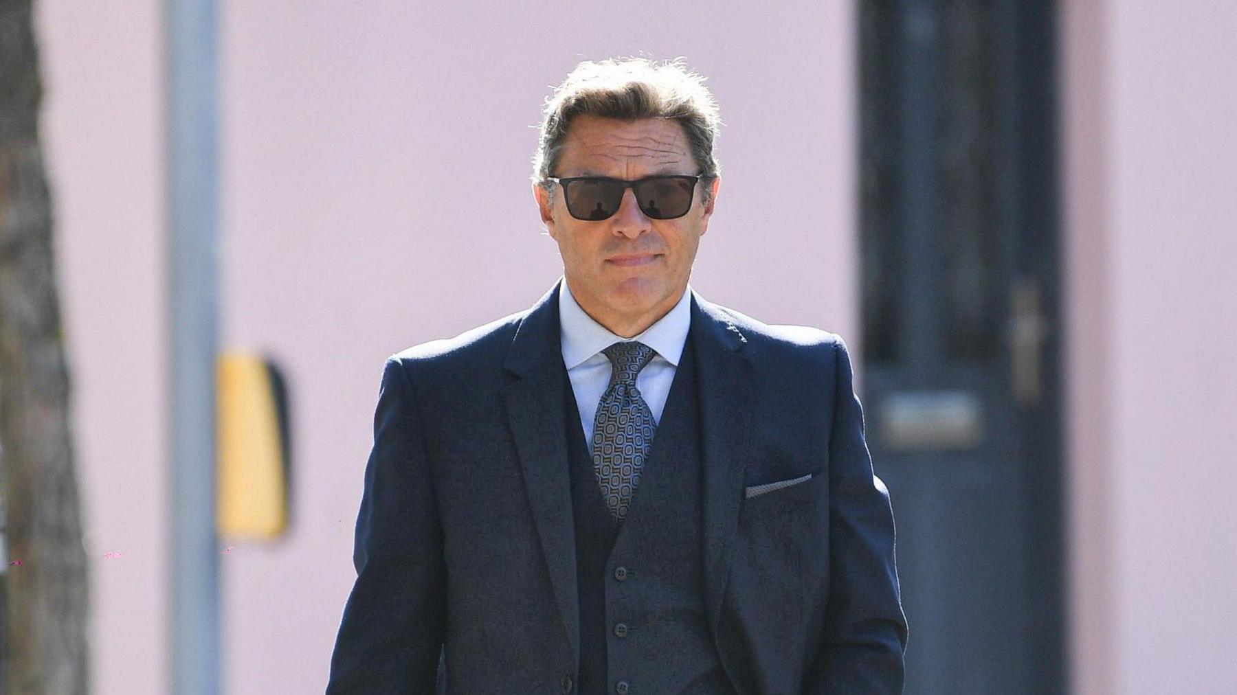 David Steenson is walking into Jersey's Magistrates Court. He is wearing a dark three-piece suit and sunglasses.