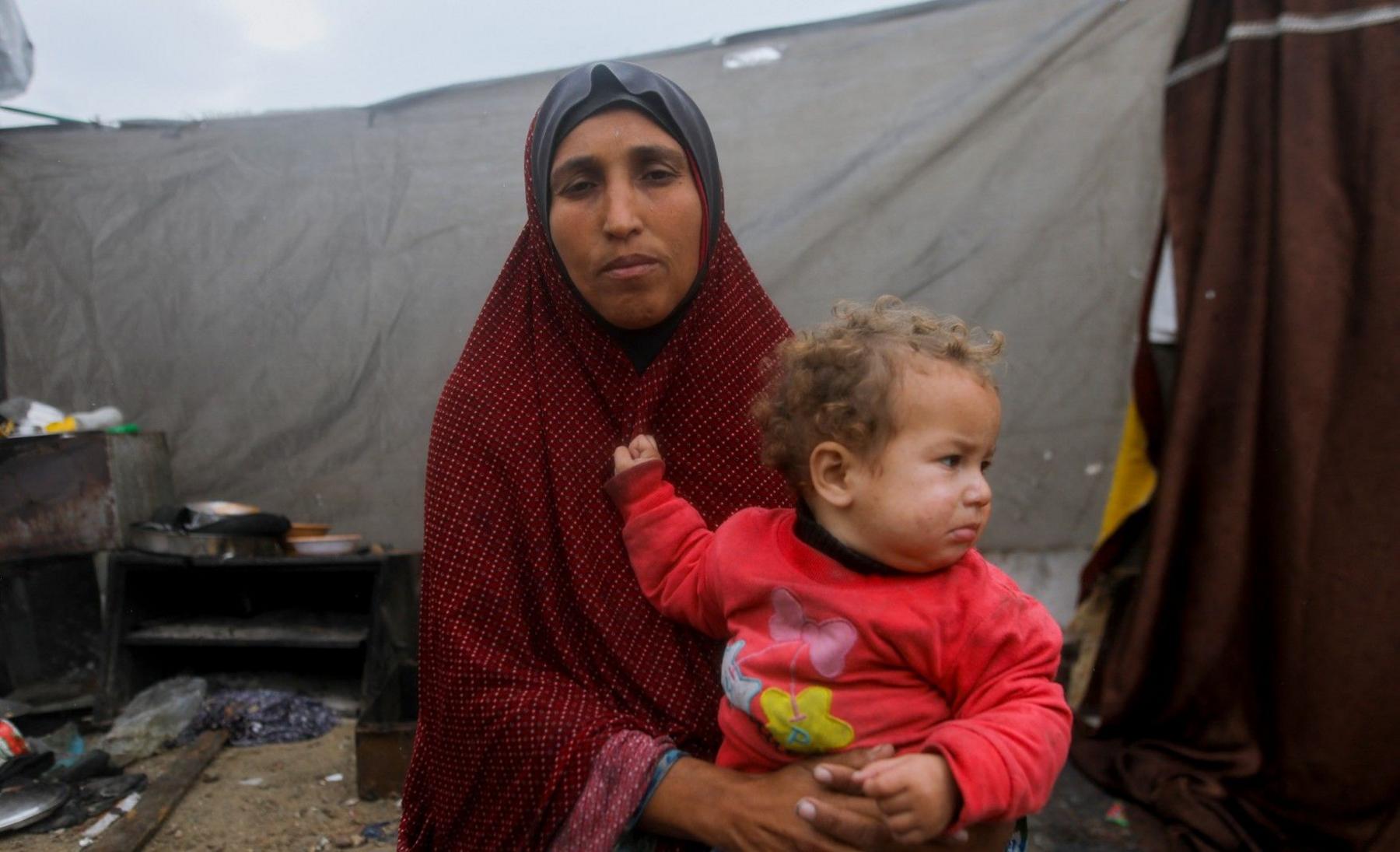 A Palestinian woman is seen holding her child outside their makeshift shelter in Jabalia, northern Gaza