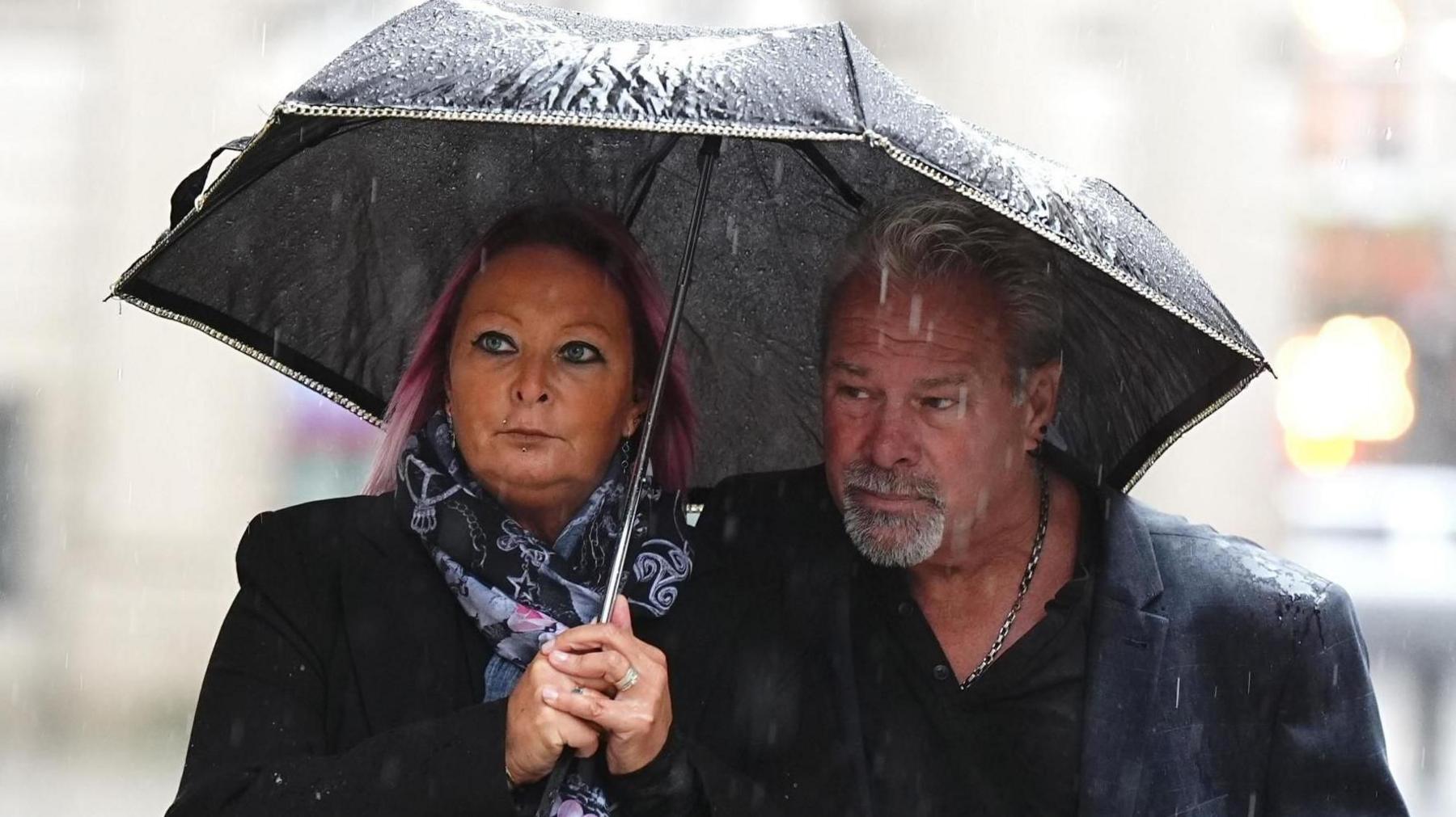 Harry Dunn's mother and stepfather dressed in black and both huddling under an umbrella on a rainy day