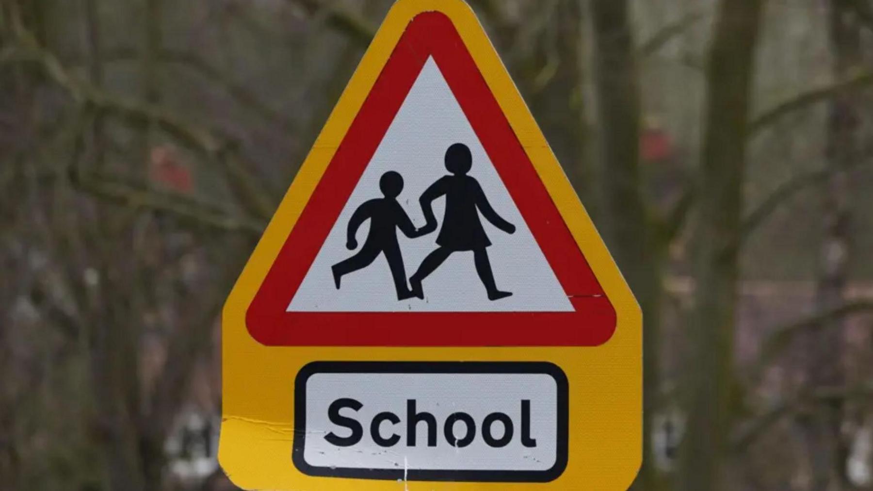 A school road sign showing a parent and child holding hands in silhouette.