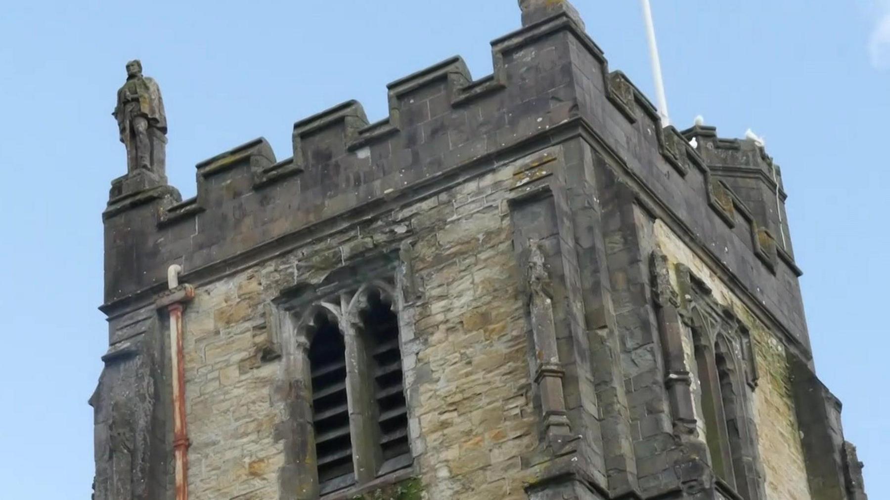 A close up of the top of the church tower. A figure of a man can be seen on the top of the turret.