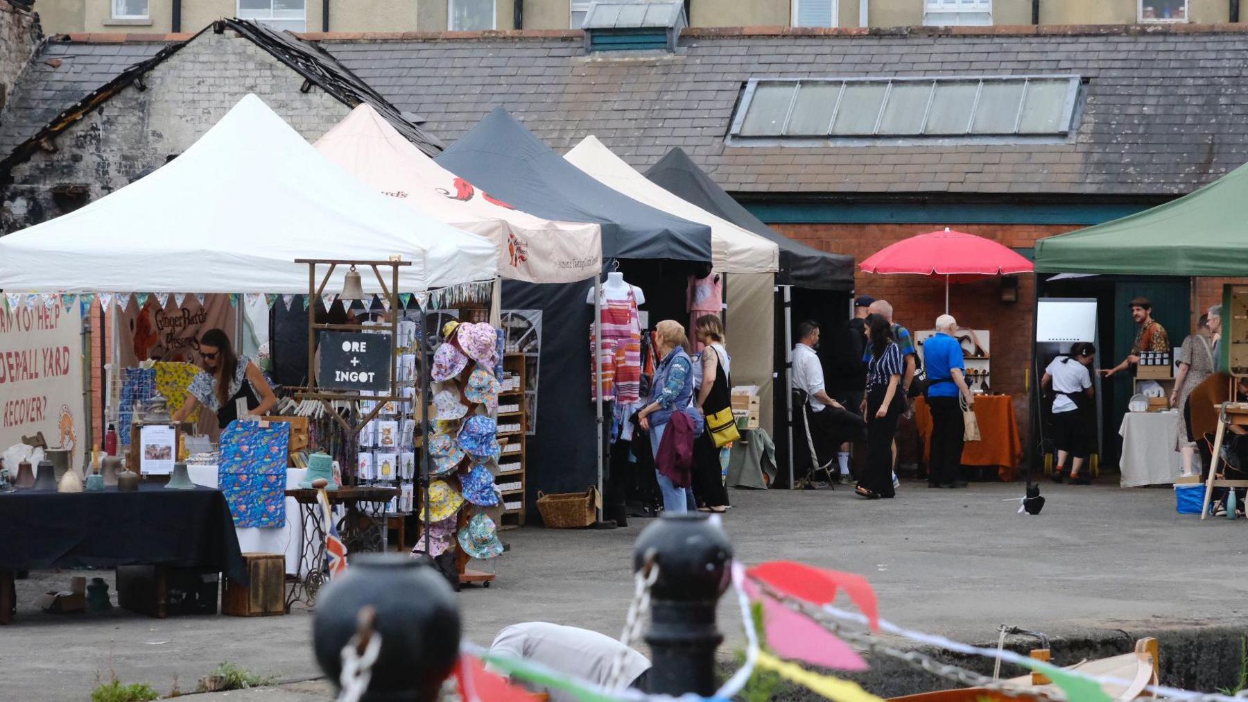 People gathered looking at stalls selling hats, clothes, prints and ceramics