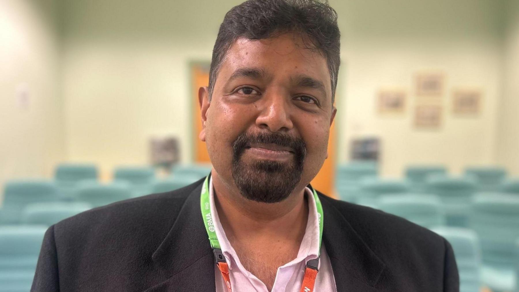 Prakash Thiagarajan, who is wearing a black suit jacket over a pink open-necked shirt, standing in a lecture theatre.