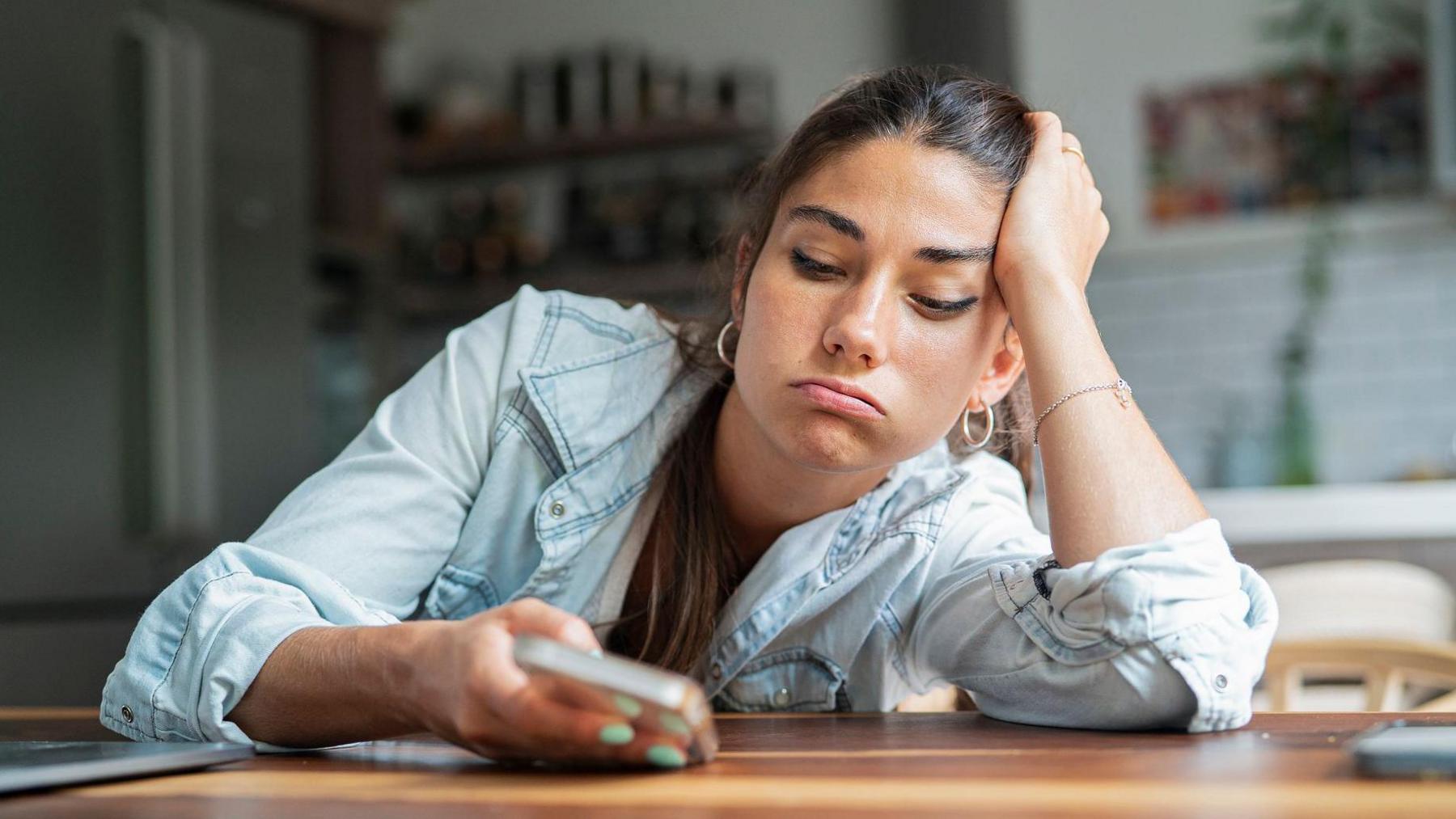 A bored young adult woman looking at her smartphone