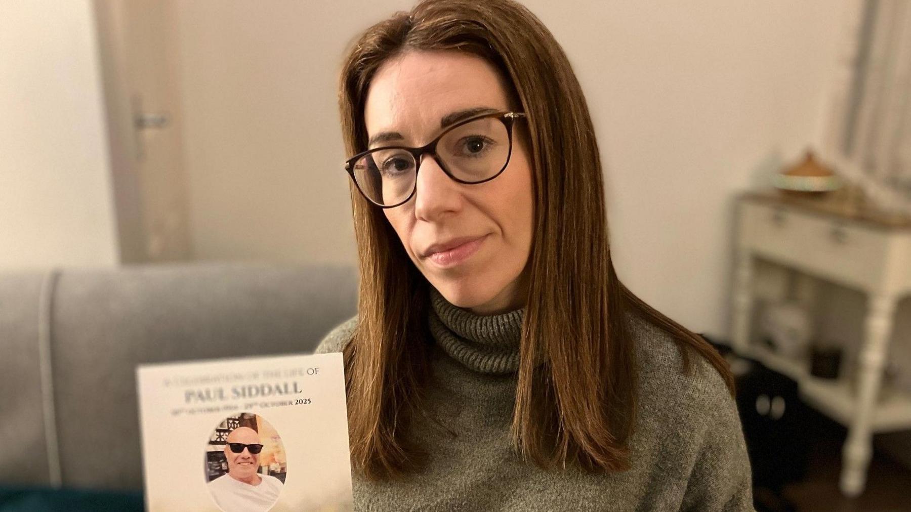 Sam Siddall, who wears glasses and has long brown hair, paid extra to have her father buried at Southern Cemetery. She is holding a funeral card with her late dad's photograph on the front.