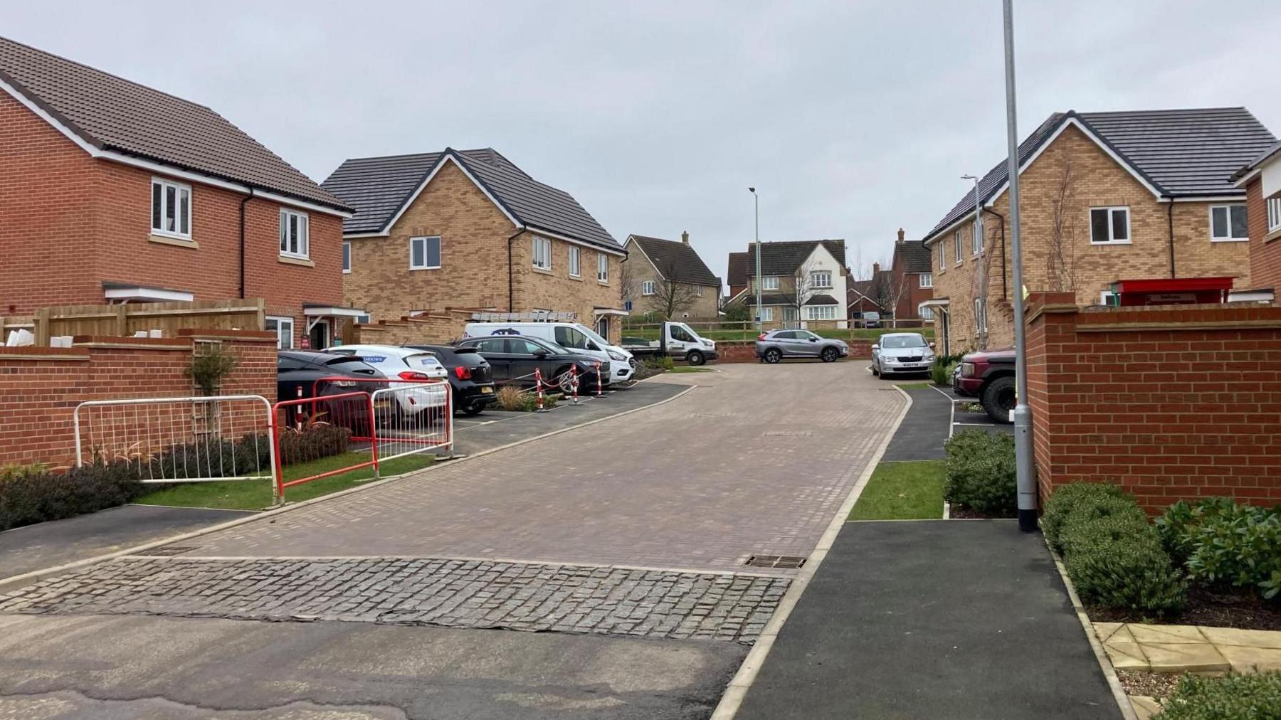 Leveret Gardens with new-build brick homes on both sides of the road. Numerous cars are parked.