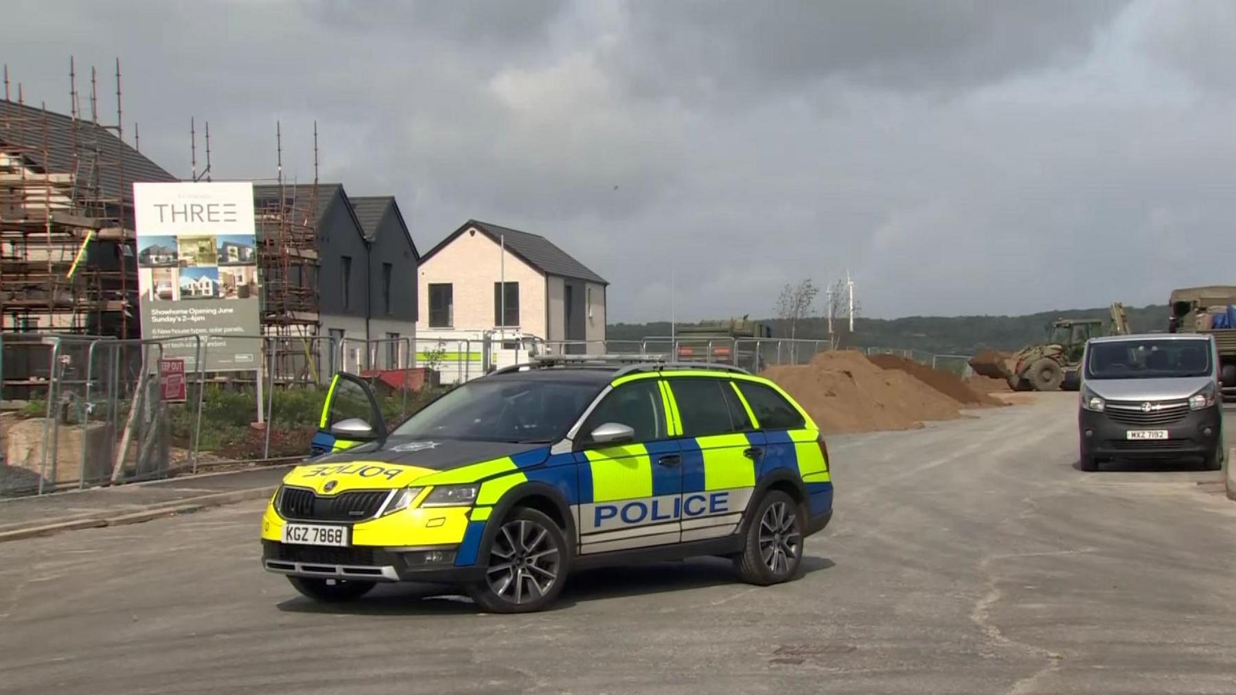 Police car in the Rivenwood housing development where army personnel are using diggers to pile sand on top of the device