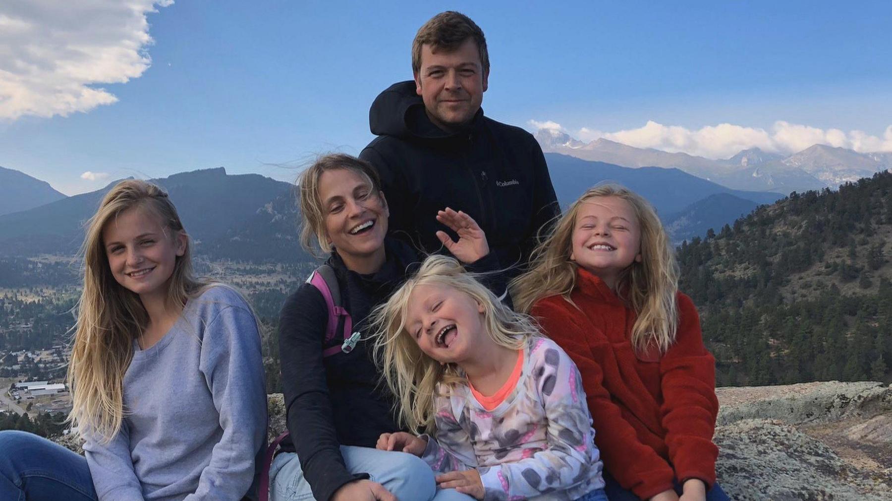 The Bastion-Strong family are pictured on a walking trip and there are mountains and forests in the background. Chris is smiling as Katie and the three girls are laughing.