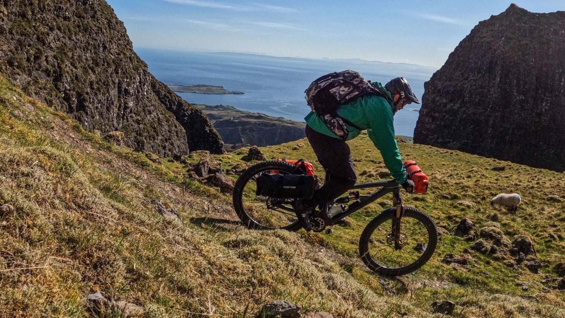 A person on a mountain bike rides down a grassy hill overlooking a body of water.