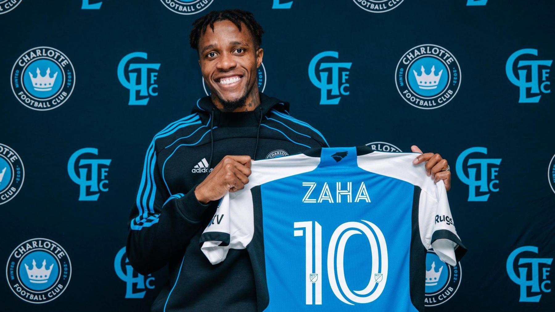 Wilfried Zaha holds up a Charlotte FC shirt 