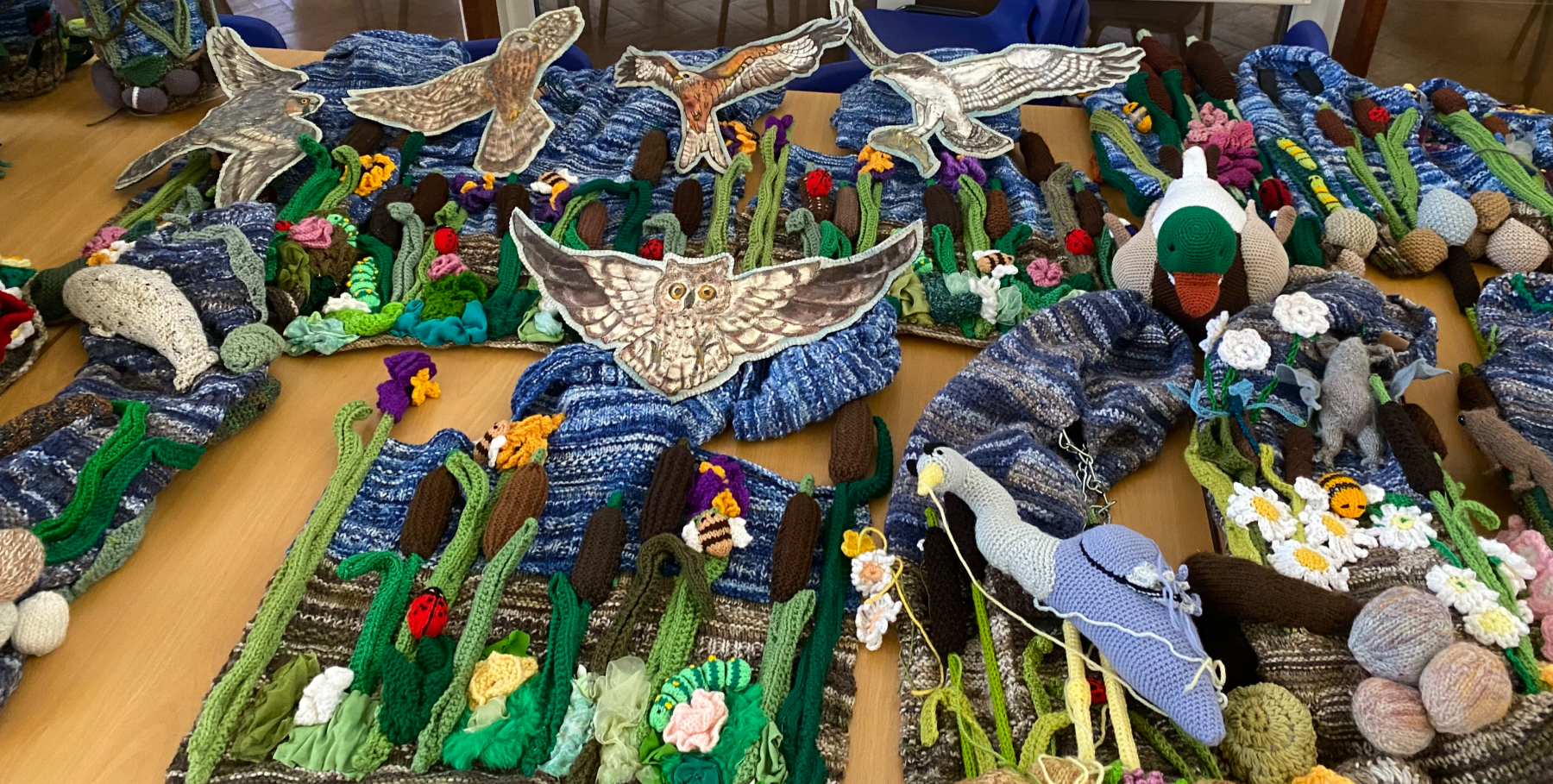 A river scene, made out of fabric, on the floor, showing owls, birds, ducks, reeds, bees, and foliage. 