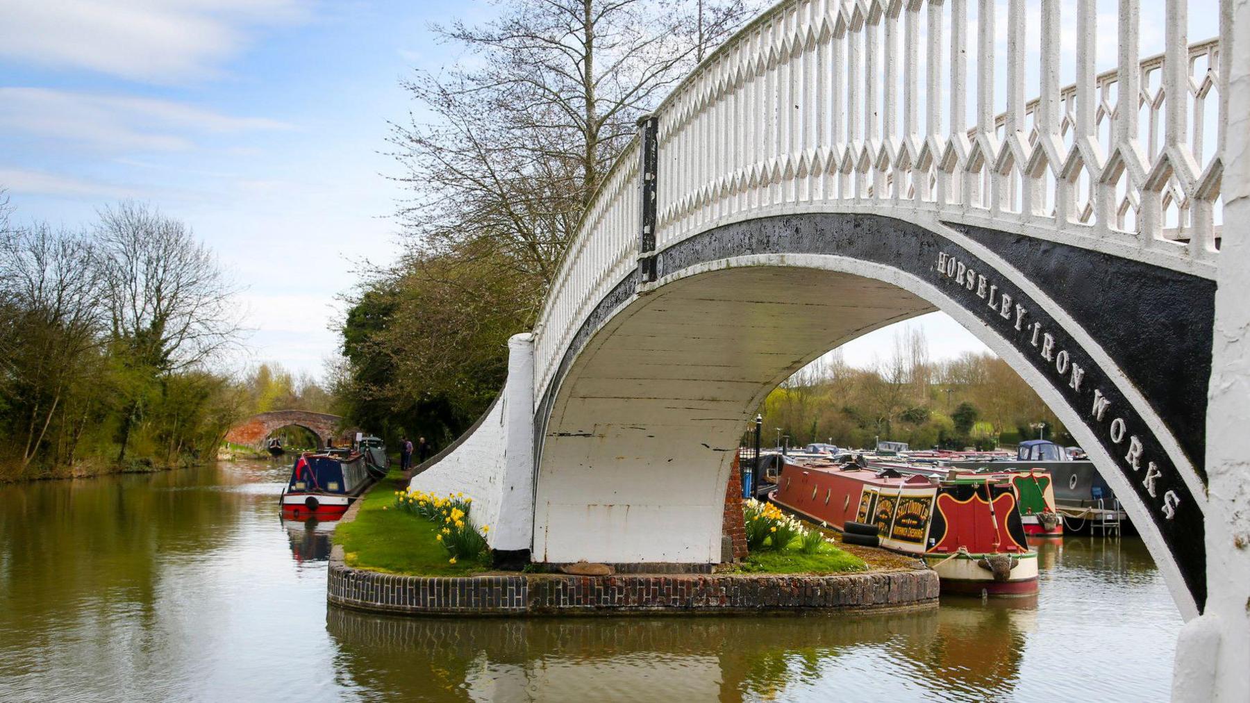 A white bridge with two red and orange boats sailing alongside it in the canal. 