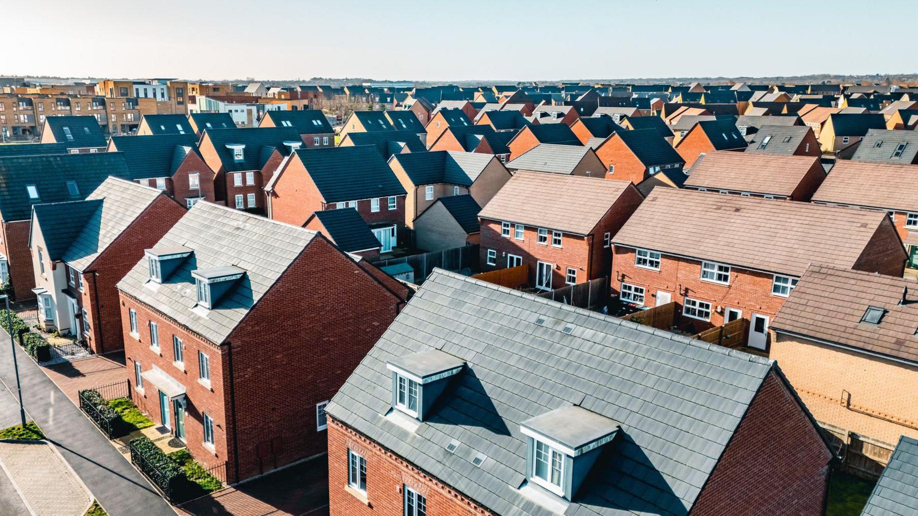 An aerial view of a group of red brick houses. The sky is blue. 