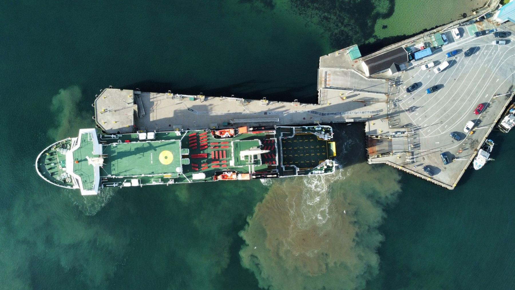 A top down drone shot of a large ship with green decks berthing at a pier