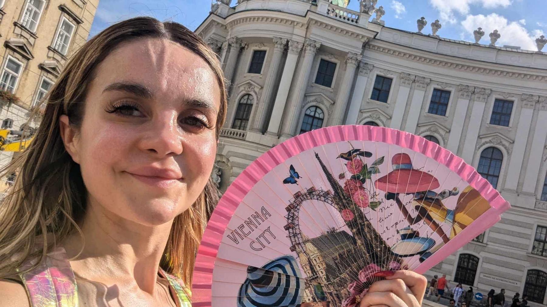 Girl with blonde hair taking a selfie with a Vienna city fan 