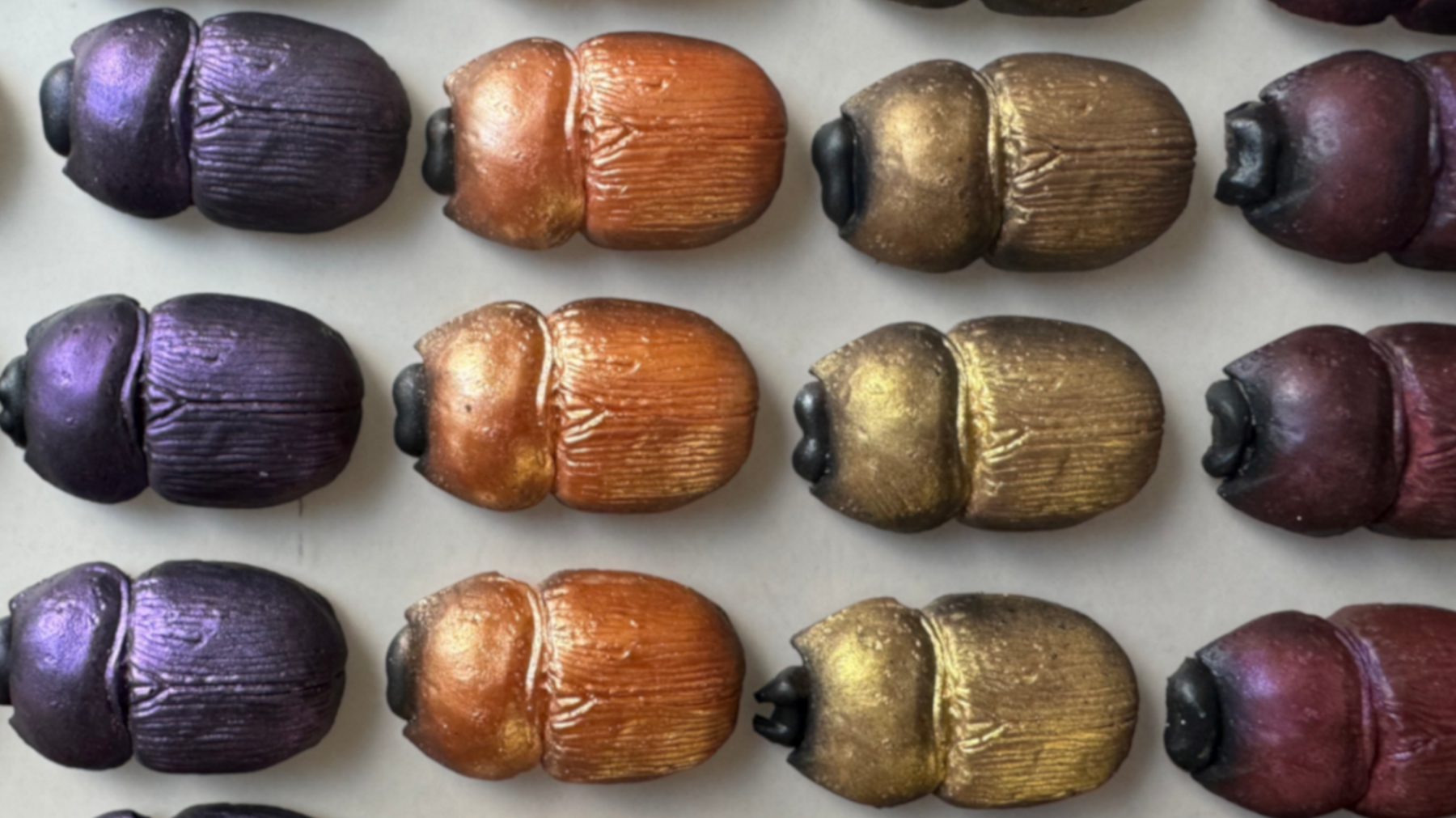 Rows of coloured beetles which have been created out of chocolate. The confectionary has been coloured with purple, orange, gold and red shimmers.