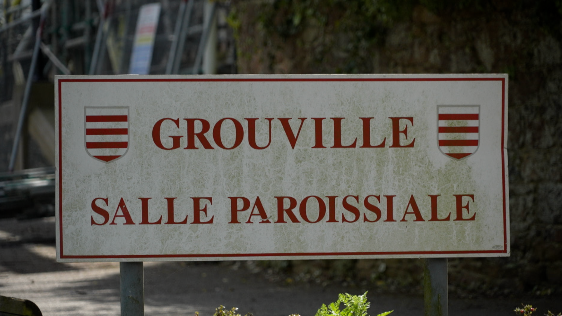 A sign outside of a building which says 'GROUVILLE / SALLE PAROISSIALE' which translates to Parish Hall in French.
