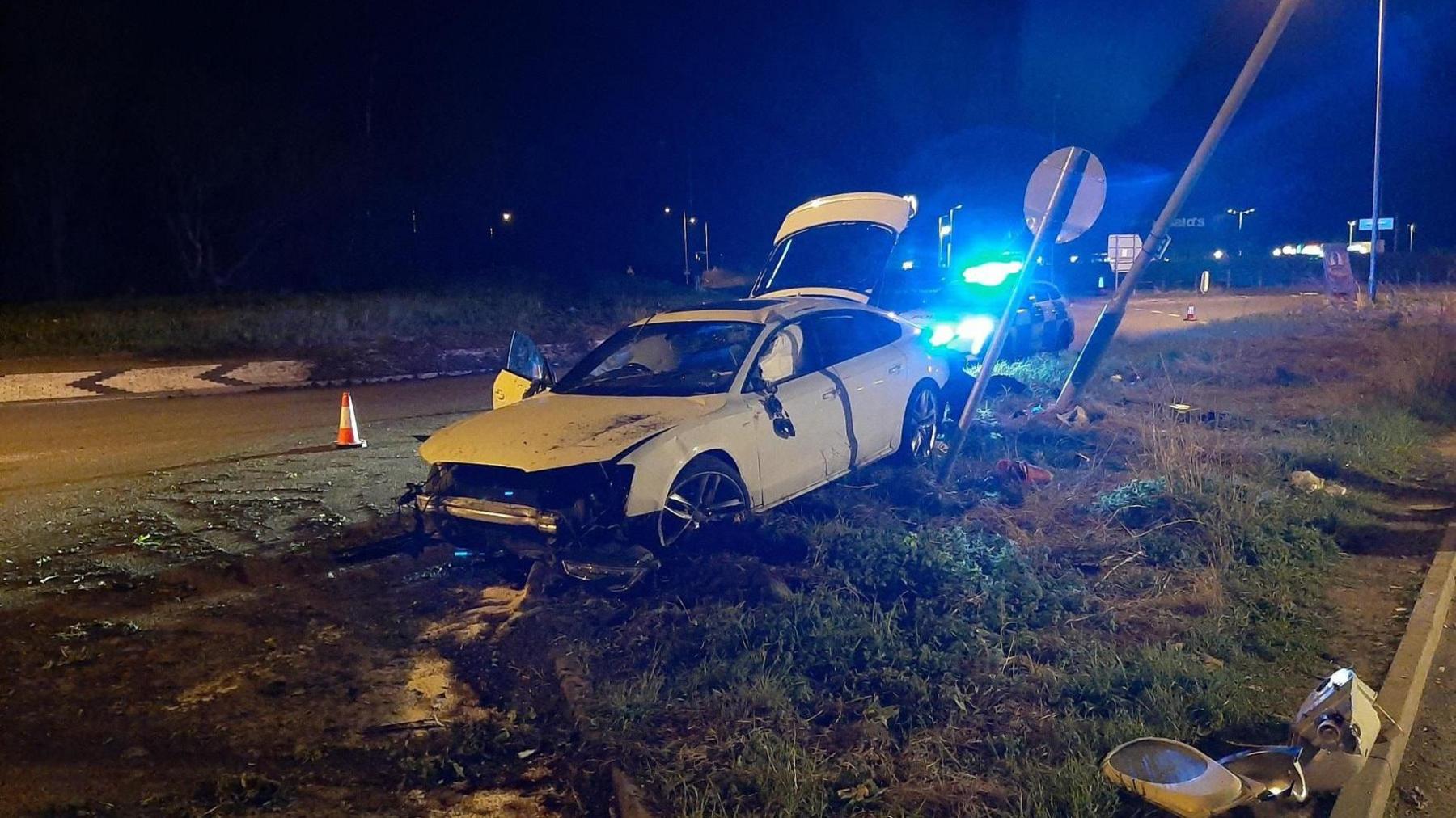 A white car that has hit a lamp post on the side of the road 