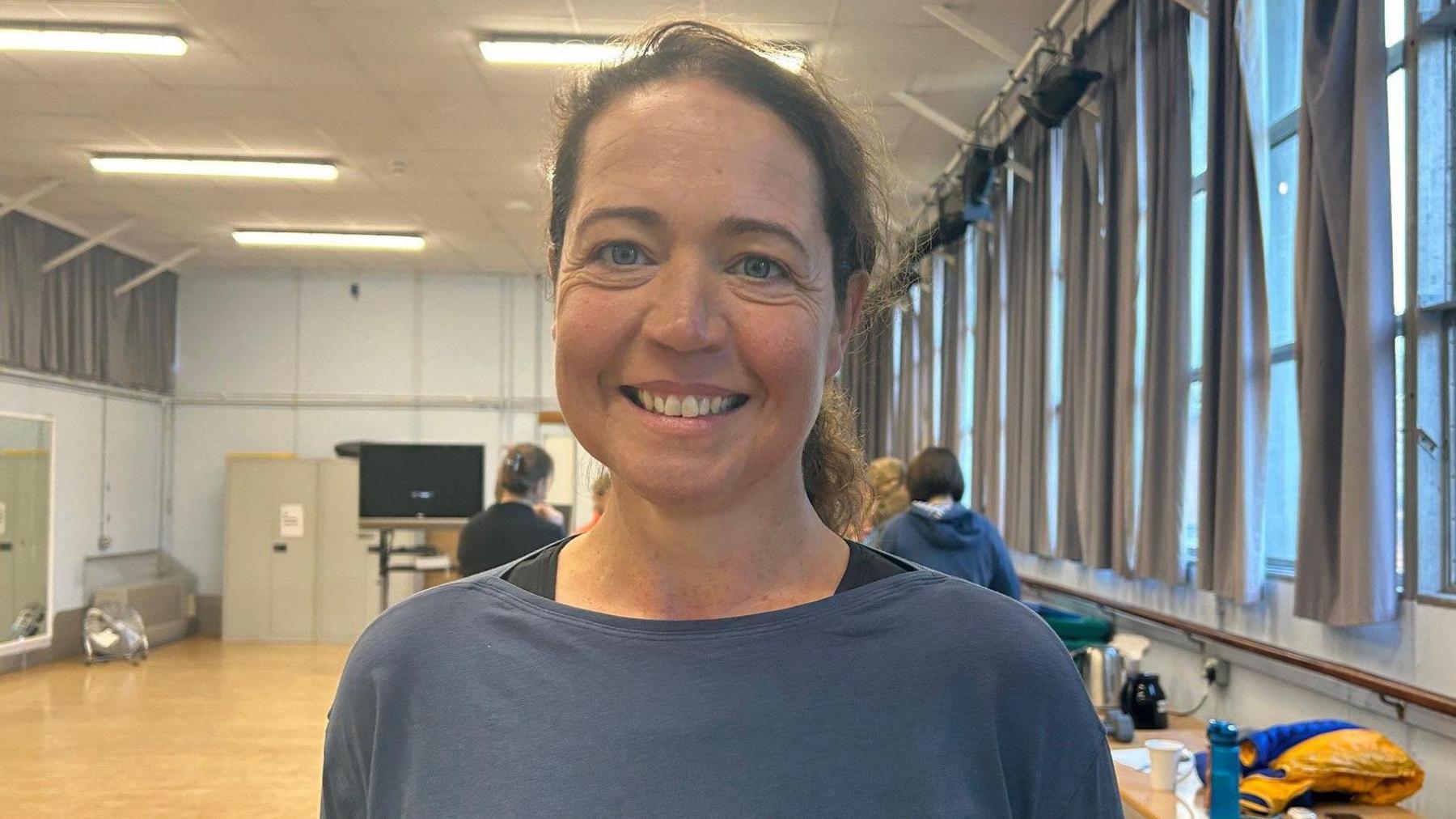 A woman who is smiling with a blue gym top.