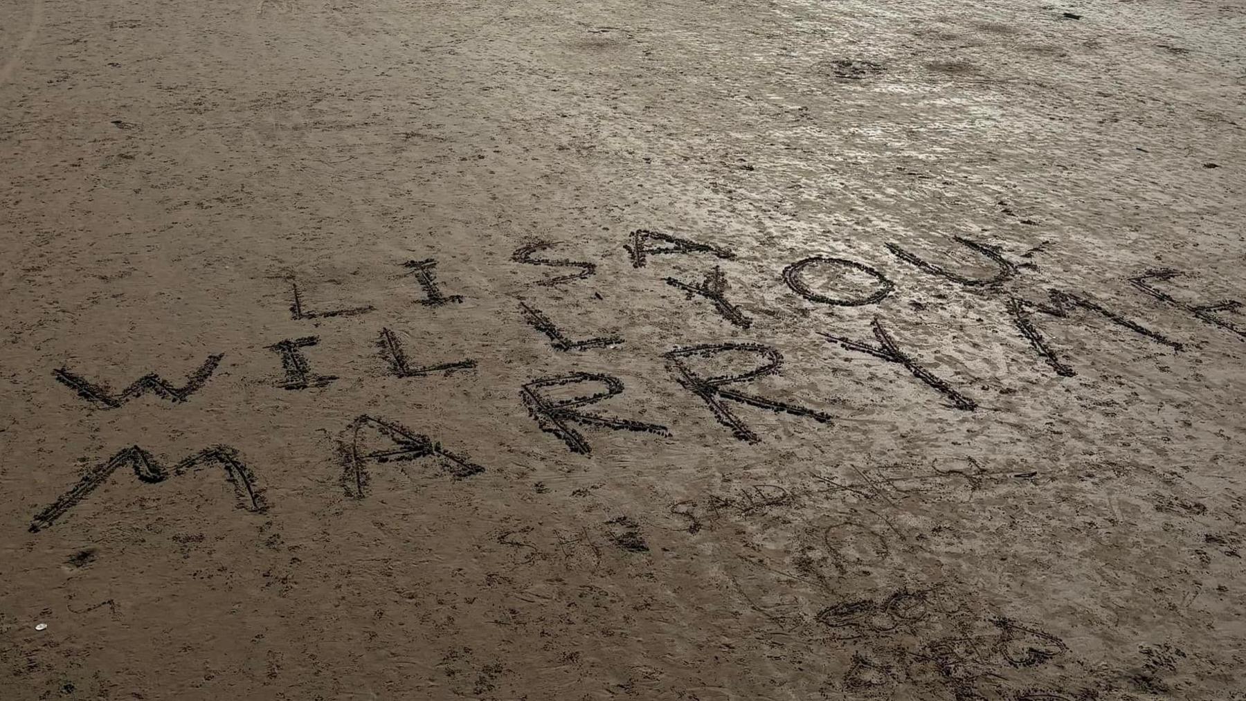 A beach with 'Lisa will you marry me?' etched into the sand