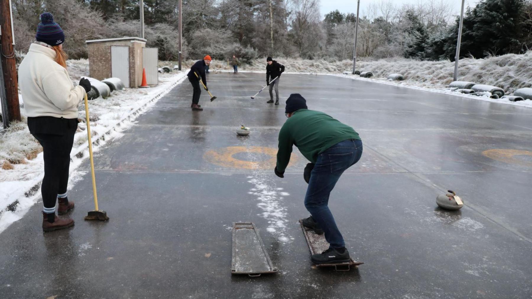 Curlers in action at the rink in Muir of Ord. There is snow lying all around in the rink.