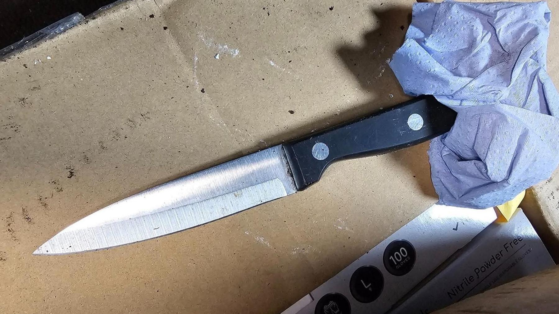 Close up of a black handled knife, resting on a cardboard box with paper towel around the handle.