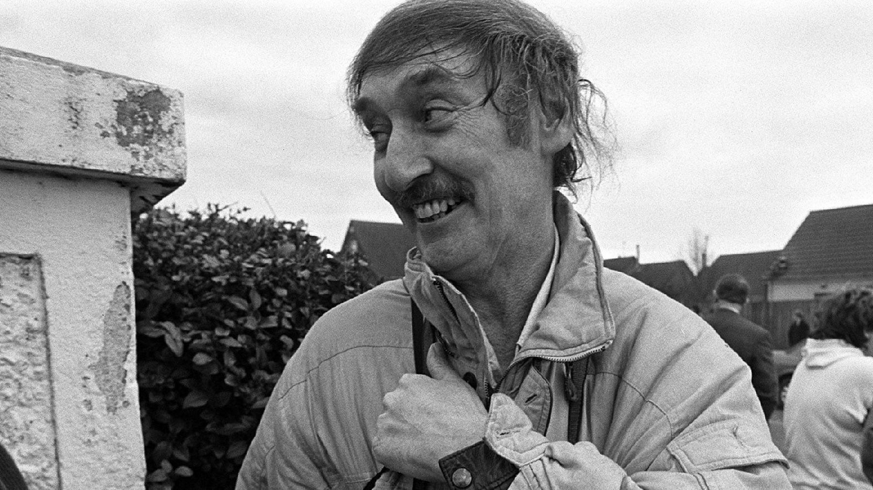 A black and white picture of Mr Murphy, has long dark hair and has a moustache. He is wearing a light coloured waterproof coat.