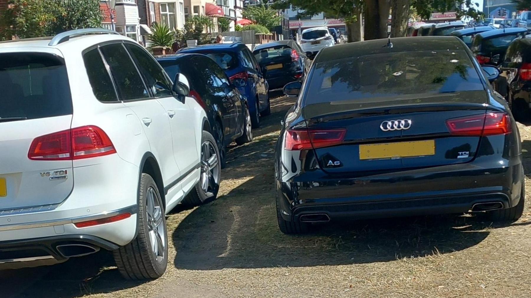multiple cars parked on a row on a pavement in the summertime
