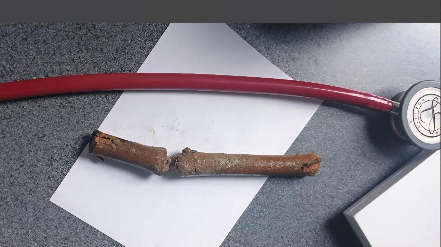 A stick which is on a white piece of paper on a grey desk, next to what looks like a red stethoscope.