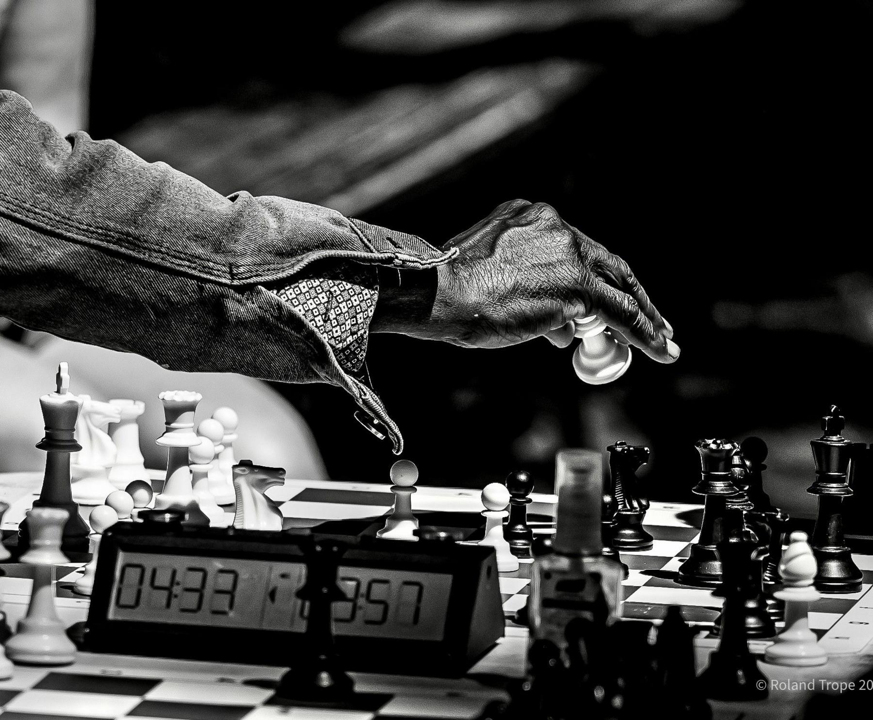 A close up of a hand holding a chees piece above the chess board with a timer nearby