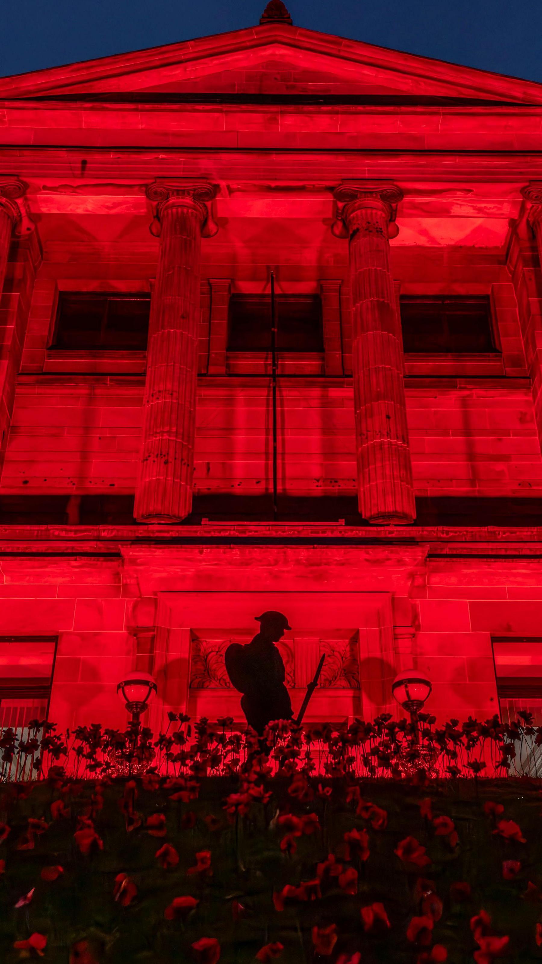 Kelvinside Academy in Glasgow lit up red with the silhouette of a soldier carrying a weapon and poppies in the foreground